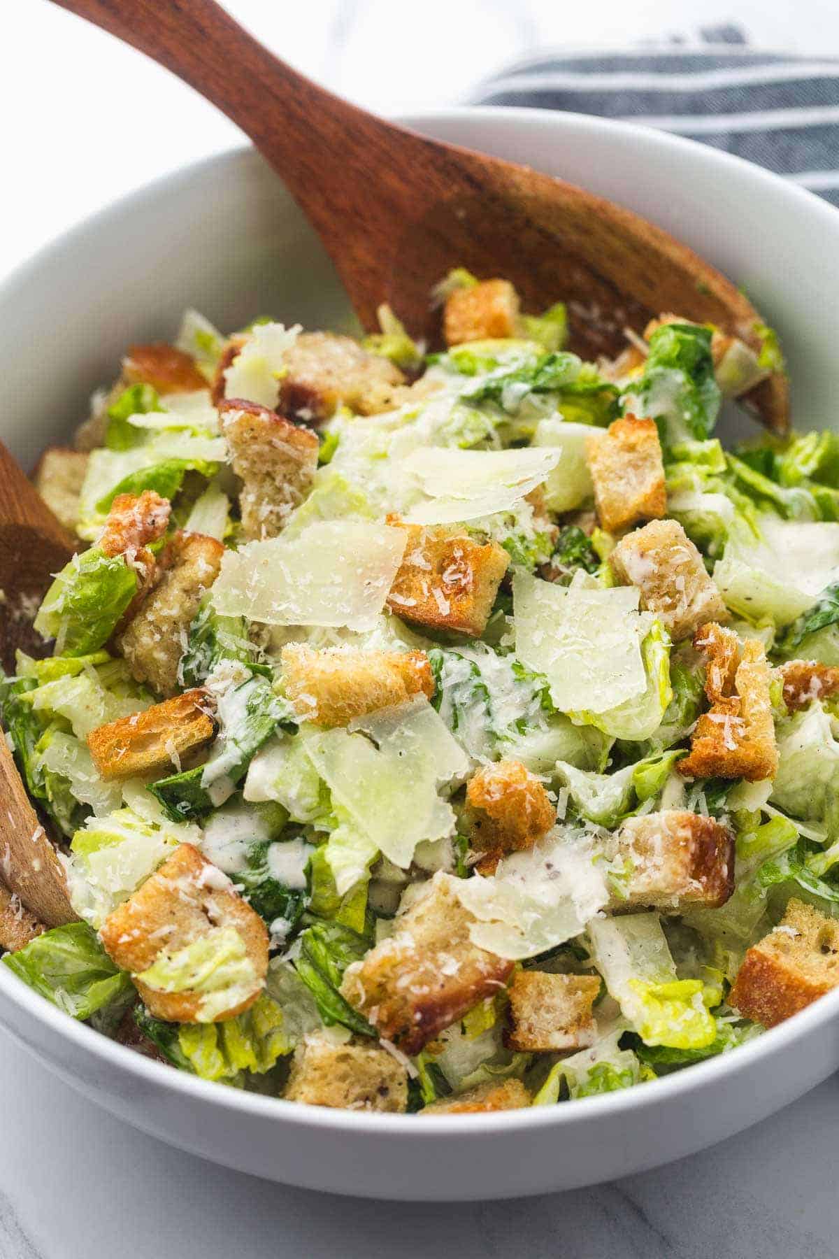 Caesar salad in a large white salad bowl, and wooden salad servers